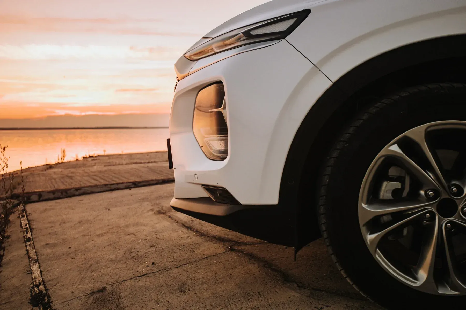 Coche blanco aparcado cerca del agua al atardecer.