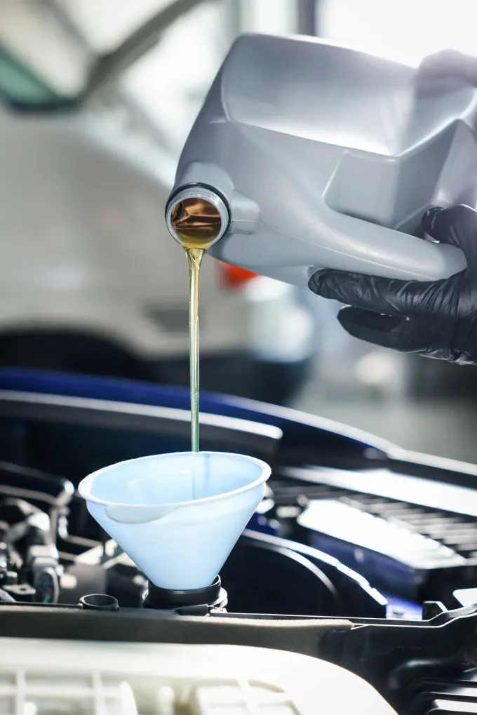 Persona vertiendo aceite de un recipiente en el motor de un automóvil usando un embudo.