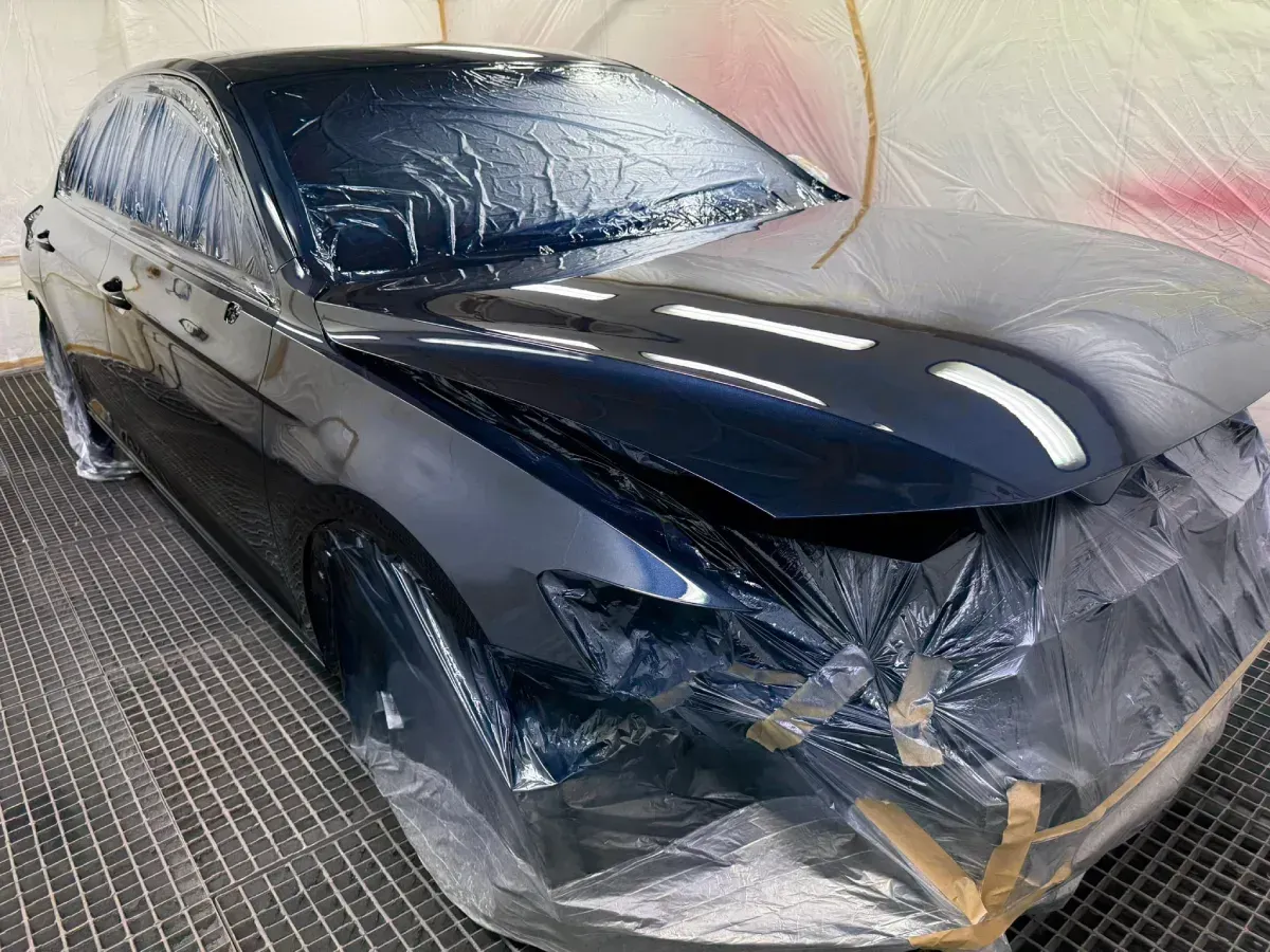 Persona con traje de protección inspeccionando la pintura de un automóvil en una cabina de pintura.