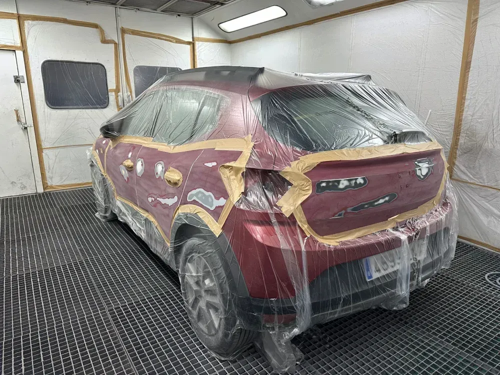Coche en cabina de pintura, parcialmente cubierto con papel y láminas de plástico.