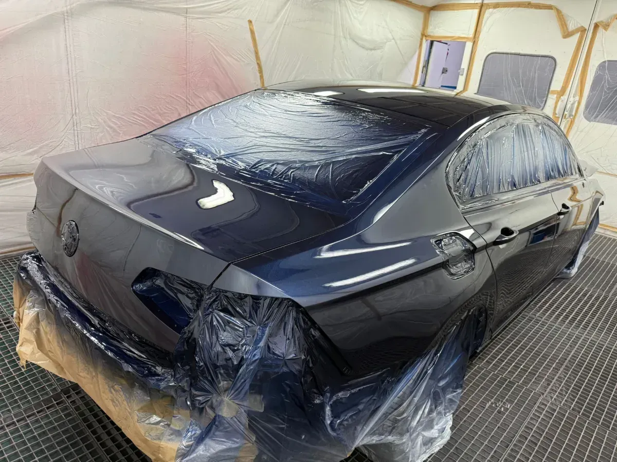 Persona con traje de protección inspeccionando la pintura de un automóvil en una cabina de pintura.