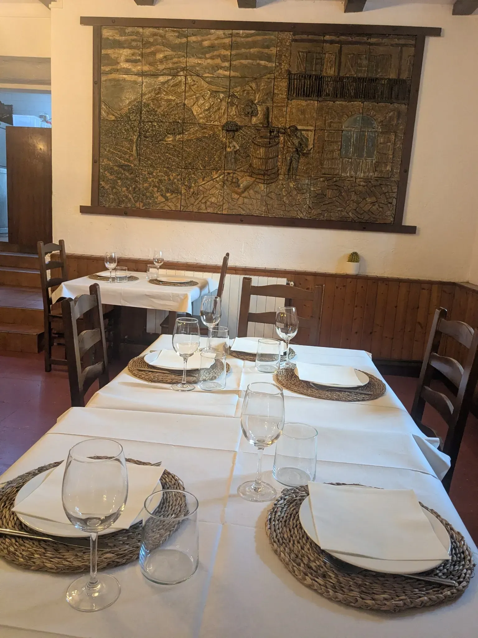 Mesa de comedor de restaurante para servir, con manteles blancos, vasos, platos y manteles individuales tejidos. 