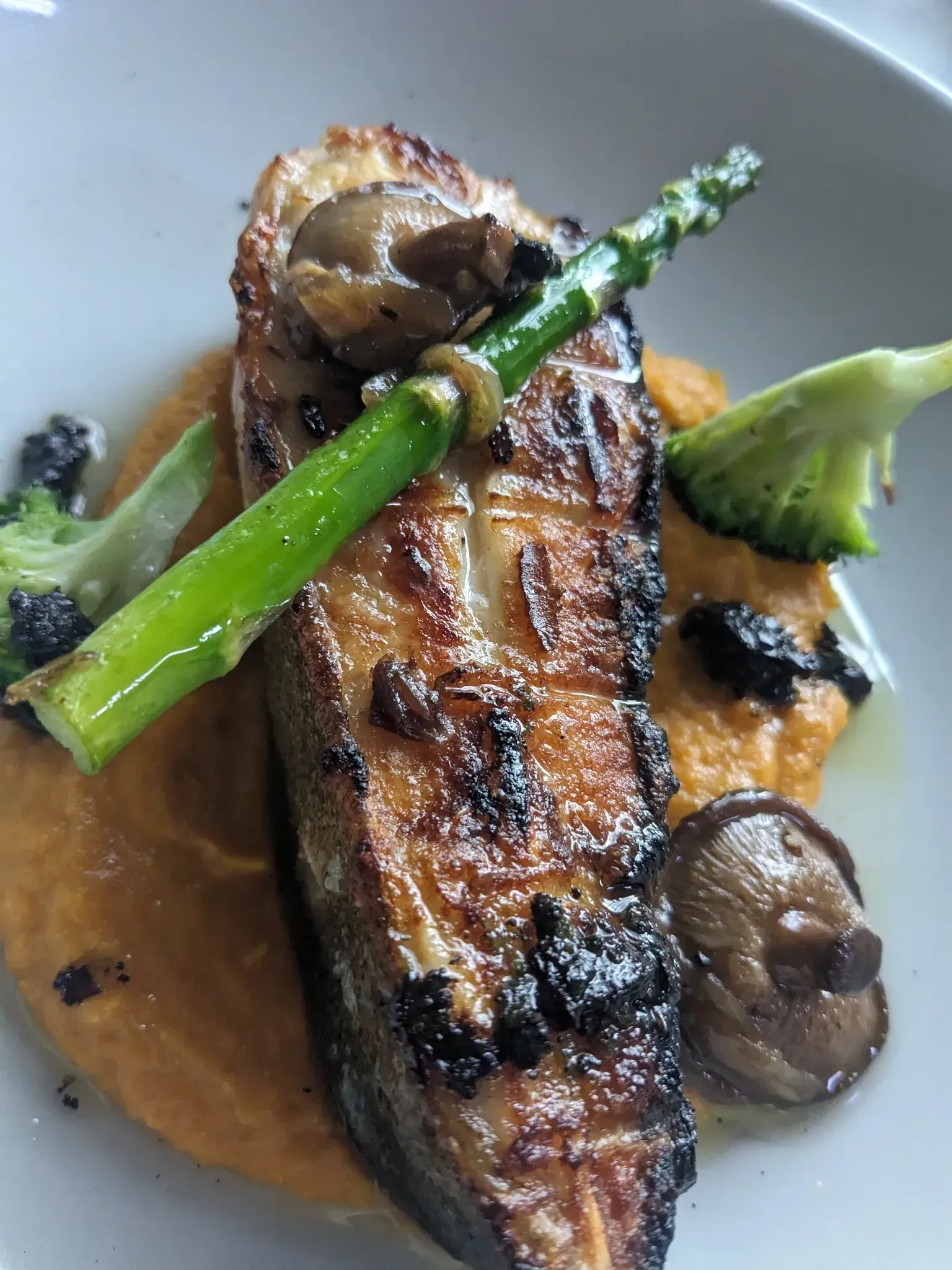 Pescado a la plancha con verduras y puré de naranja en un plato blanco.