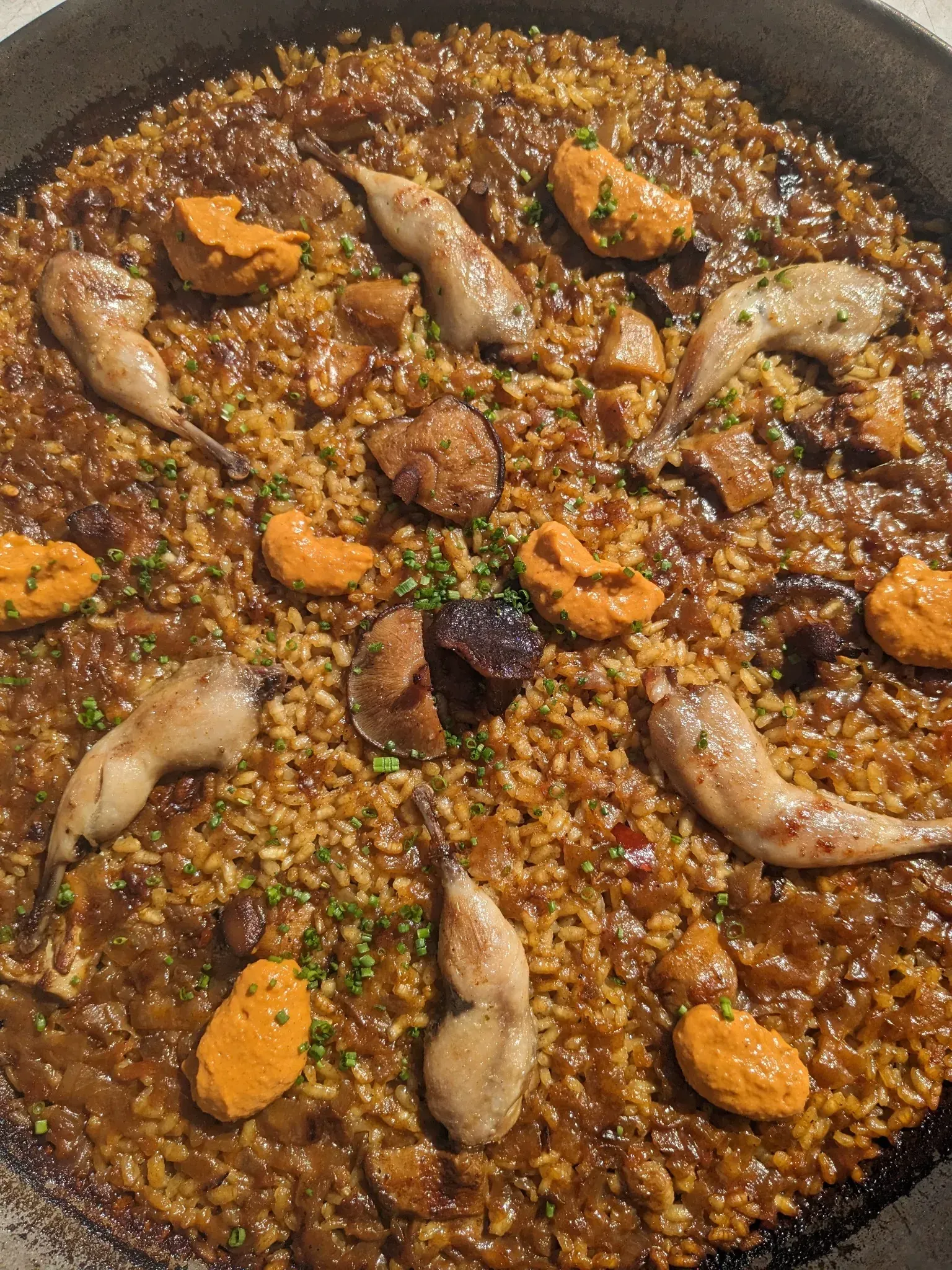 Paella con codorniz, setas y bolas de naranja en una sartén grande.