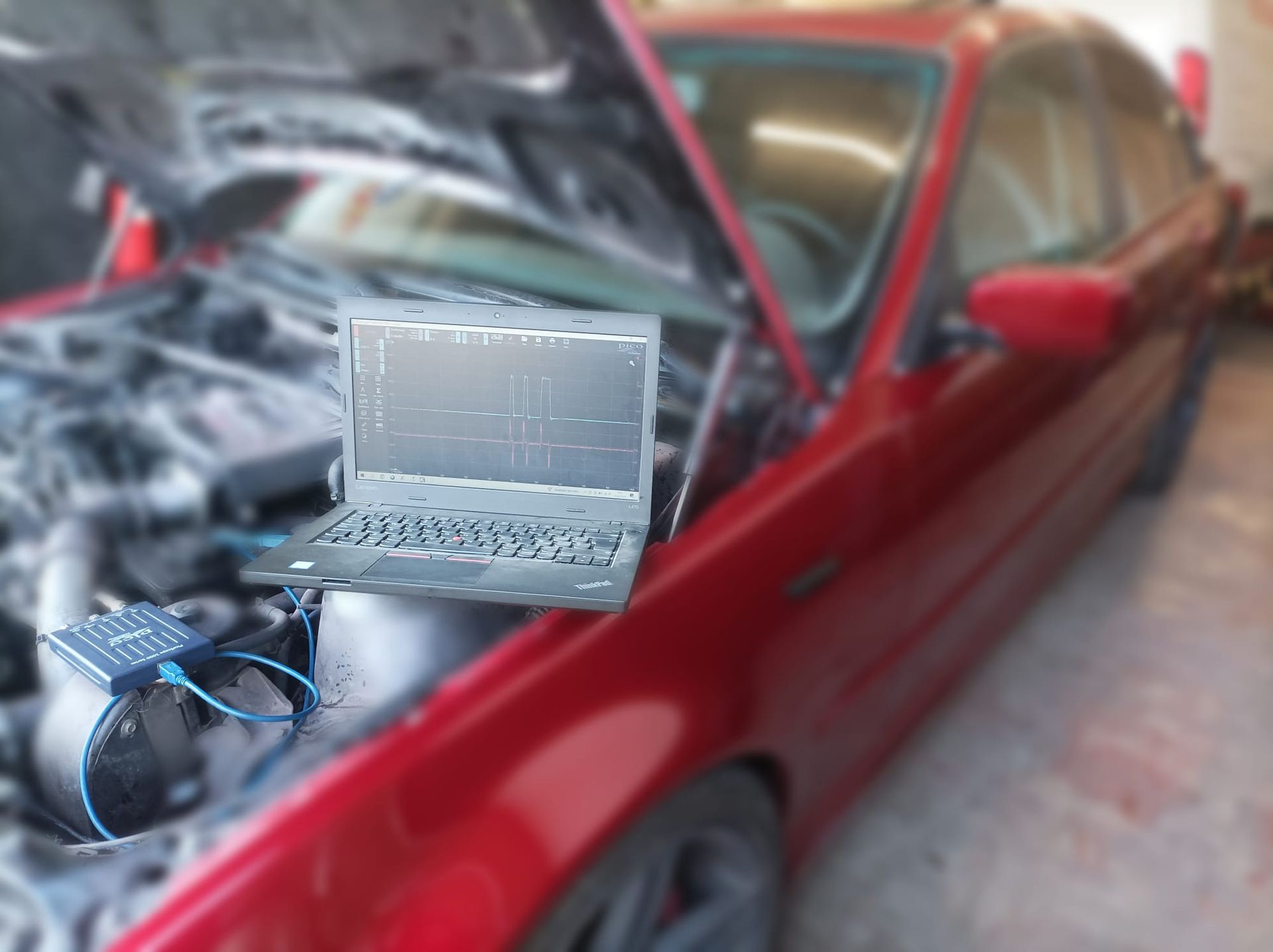 Una computadora portátil está debajo del capó de un automóvil rojo.