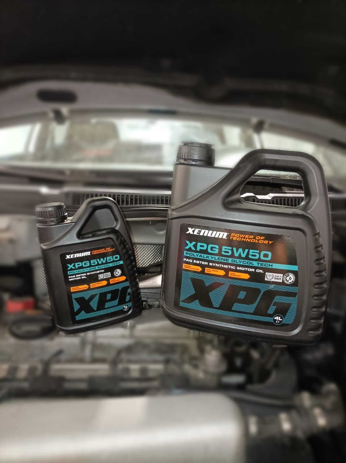 Dos botellas de aceite de motor XPG 5W50 están colocadas encima del motor de un automóvil.