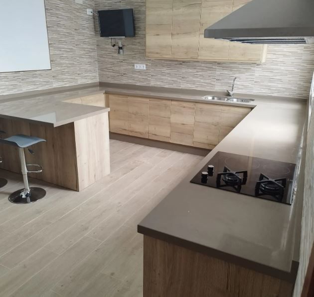 Cocina moderna con gabinetes de madera clara, isla, estufa, fregadero y protector contra salpicaduras de azulejos de piedra.