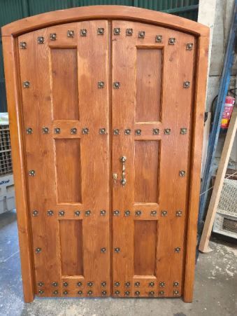 Armario de madera de dos puertas con tapa arqueada y bisagras metálicas, situado en el exterior.