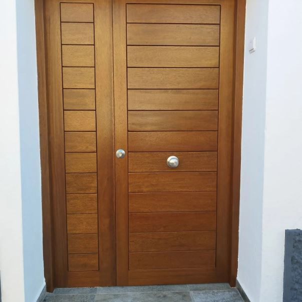 Puerta doble de madera con listones horizontales y tiradores plateados en un recibidor blanco.