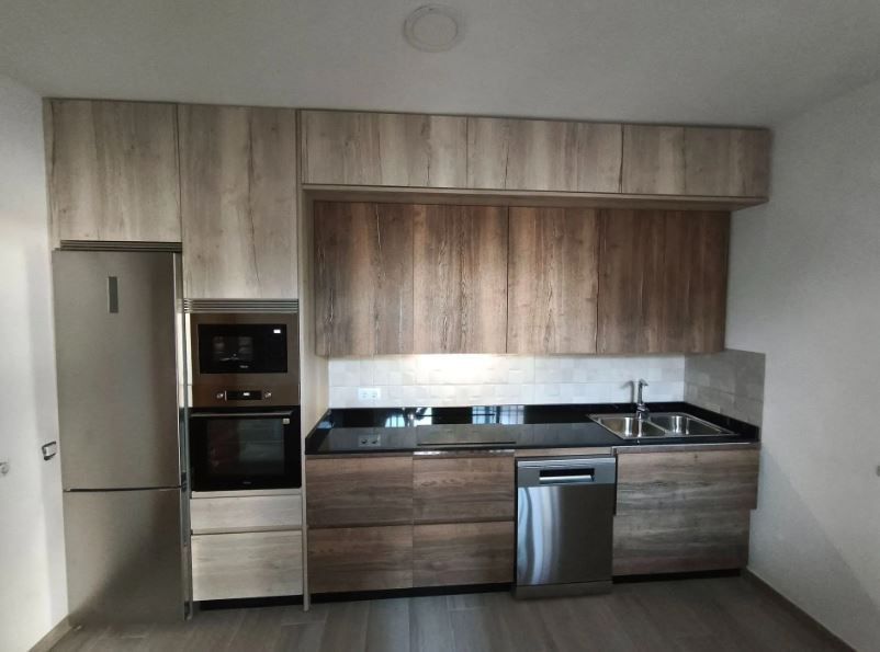 Cocina moderna con gabinetes de madera, electrodomésticos de acero inoxidable y encimera negra.