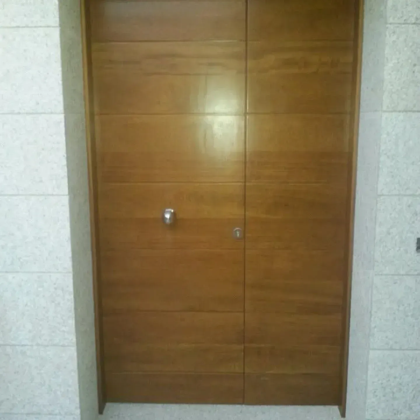 Puerta doble de madera con un pequeño pomo, enmarcada en una pared de azulejos claros.