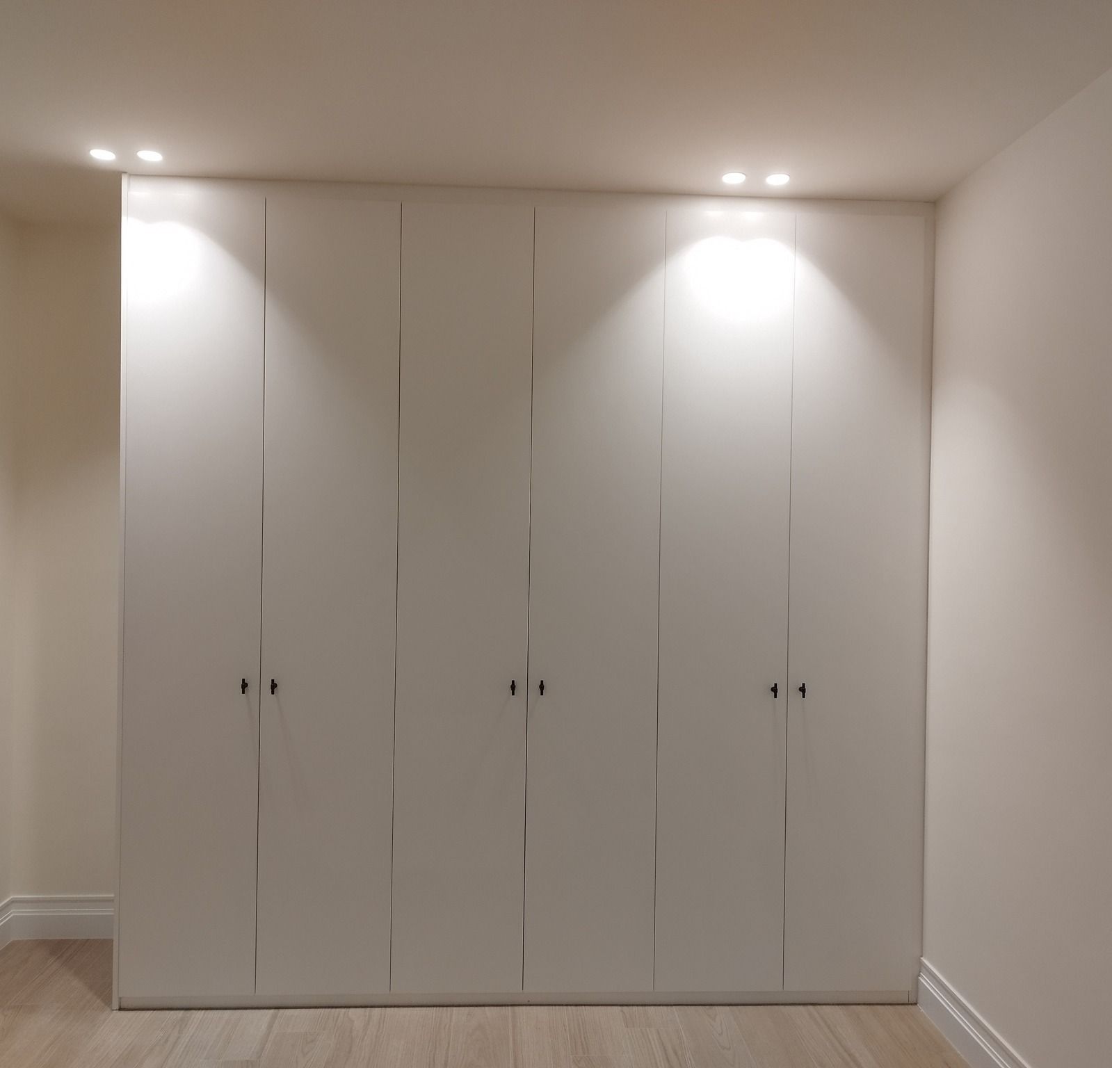 Puertas blancas de armario empotrado en una habitación minimalista con dos focos empotrados en el techo.