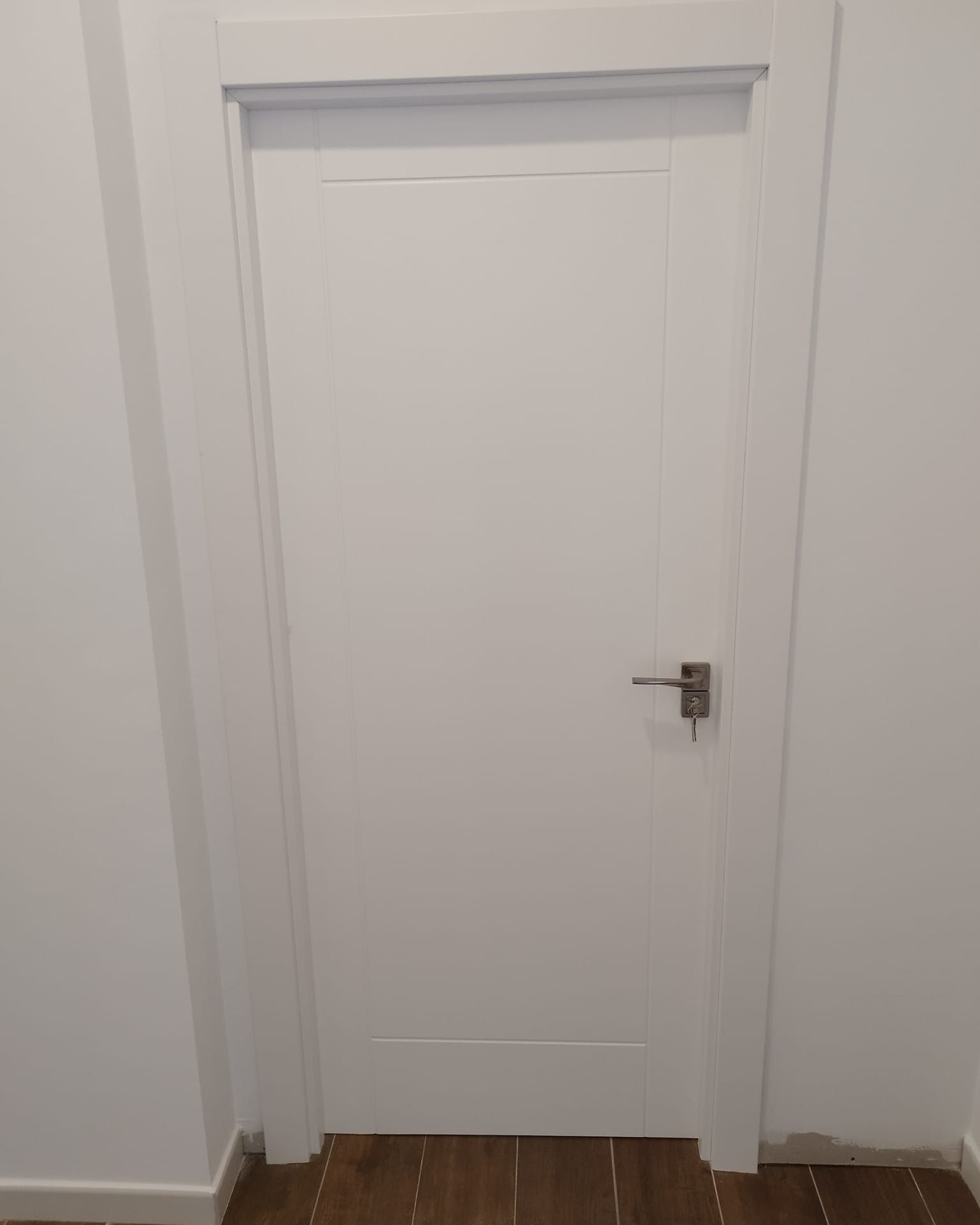 Puerta interior blanca con tirador plateado en un pasillo sencillo, cerrada.