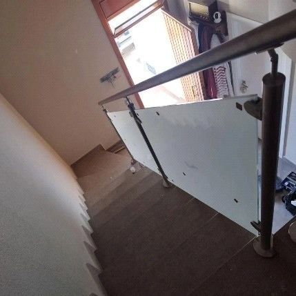 Escalera interior con moqueta marrón, barandilla de cristal y una puerta abierta en el rellano.