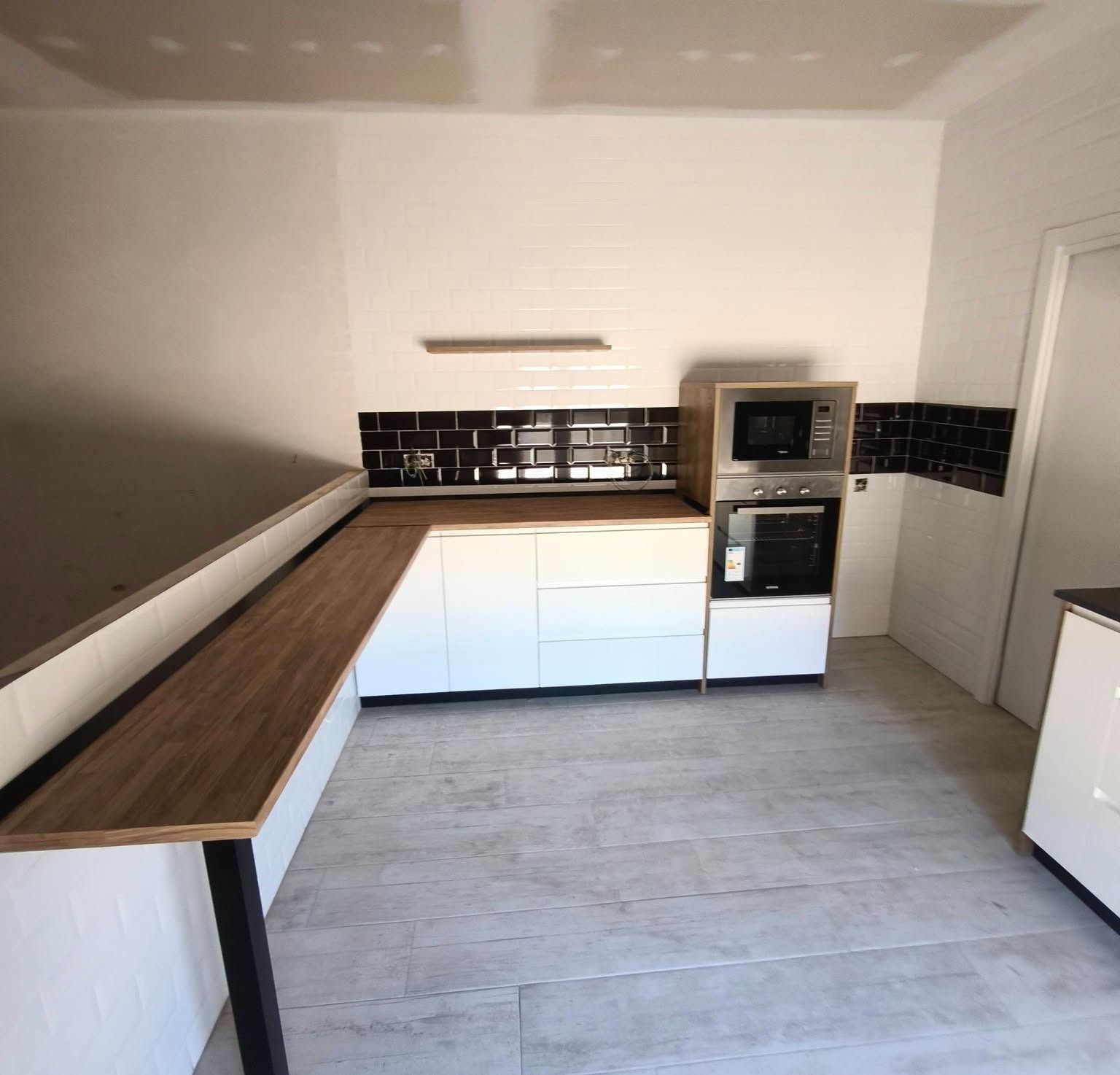 Cocina moderna con armarios blancos, encimeras de madera, salpicadero de azulejos negros y horno empotrado.