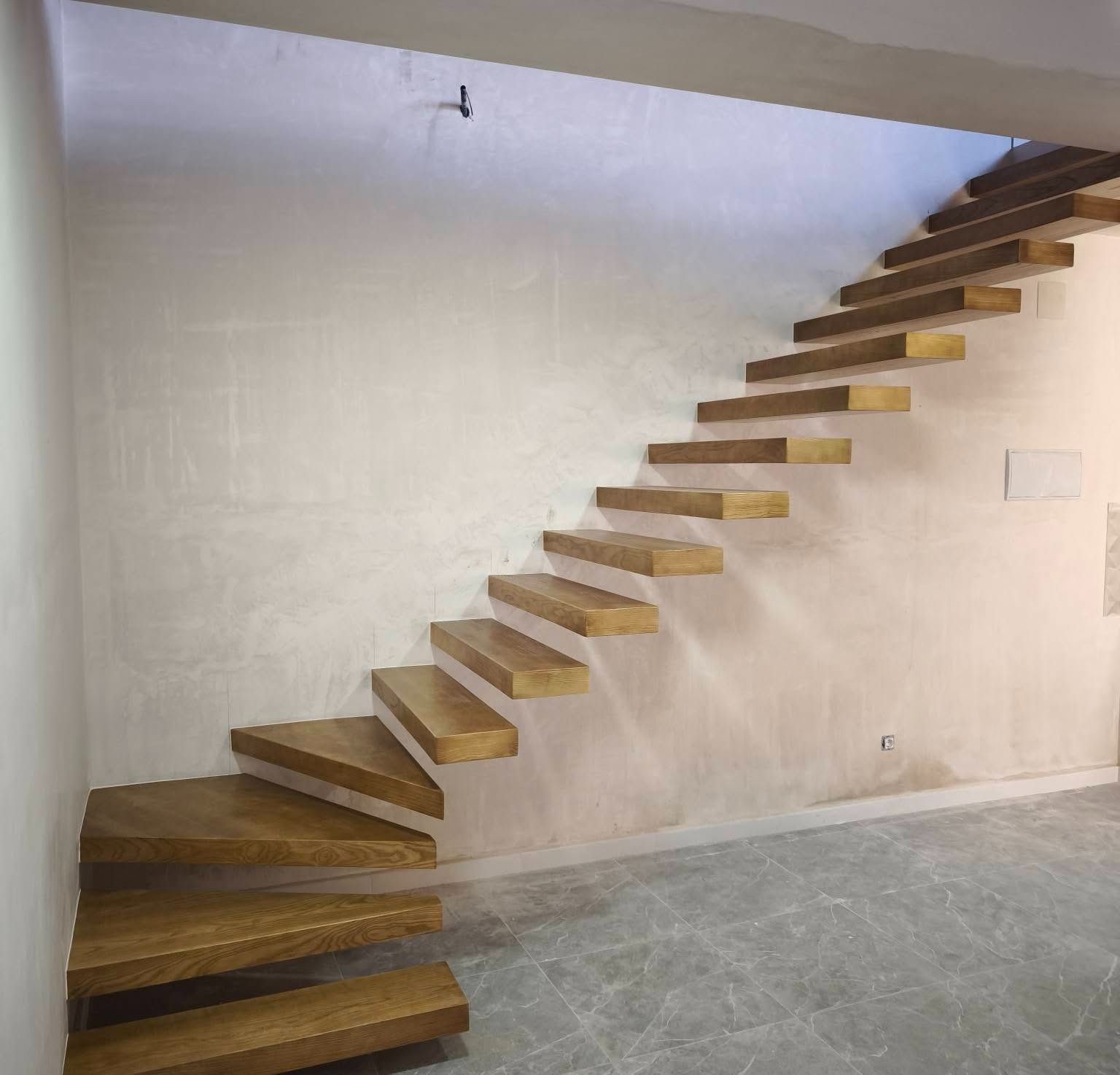 Escalera flotante de madera a lo largo de una pared blanca en una habitación de interior minimalista con suelo de hormigón.