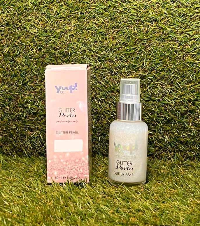 Frasco de bruma corporal rosa con purpurina junto a una caja a juego sobre un fondo de césped verde.