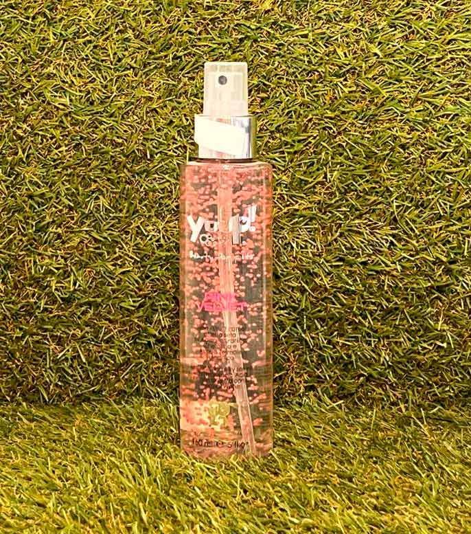 Frasco de perfume floral rosa sobre césped verde con tapón pulverizador blanco.