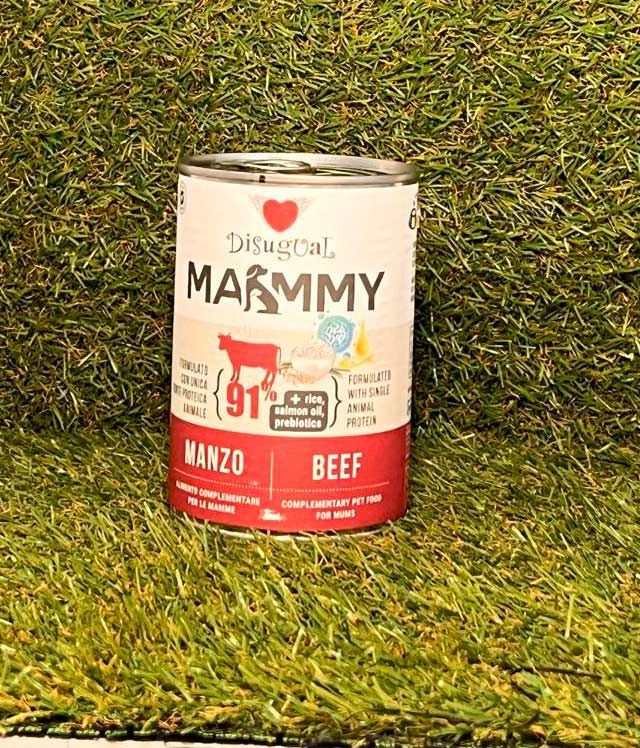 Una lata de comida para perros Disugual MAMMY sobre fondo verde, con etiqueta roja y beige que muestra el sabor a carne de res manzo.