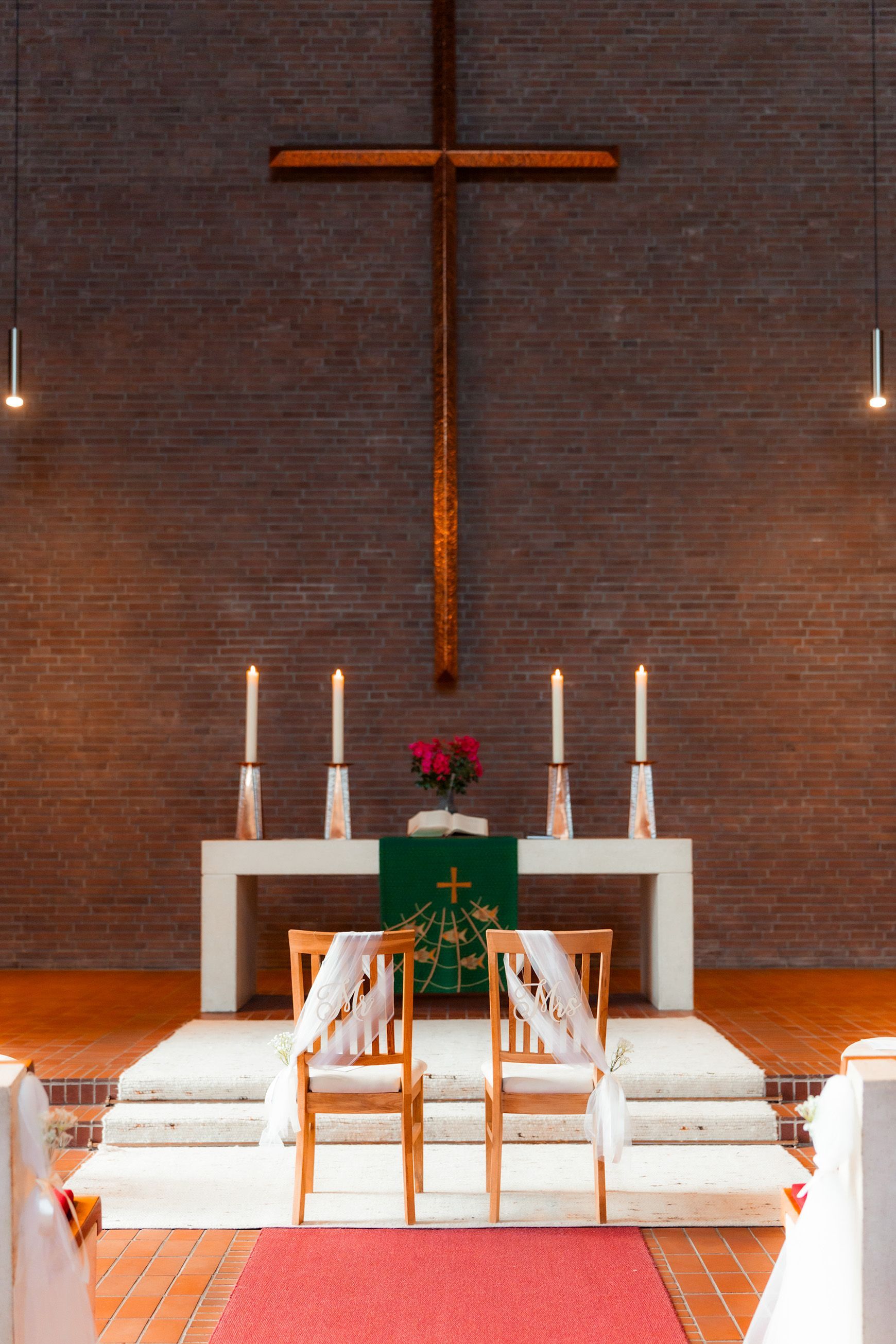 Schlichtes Holzkreuz an der Backsteinwand der Melanchthon-Kirche in Bremen, dezent beleuchtet während der Hochzeit.