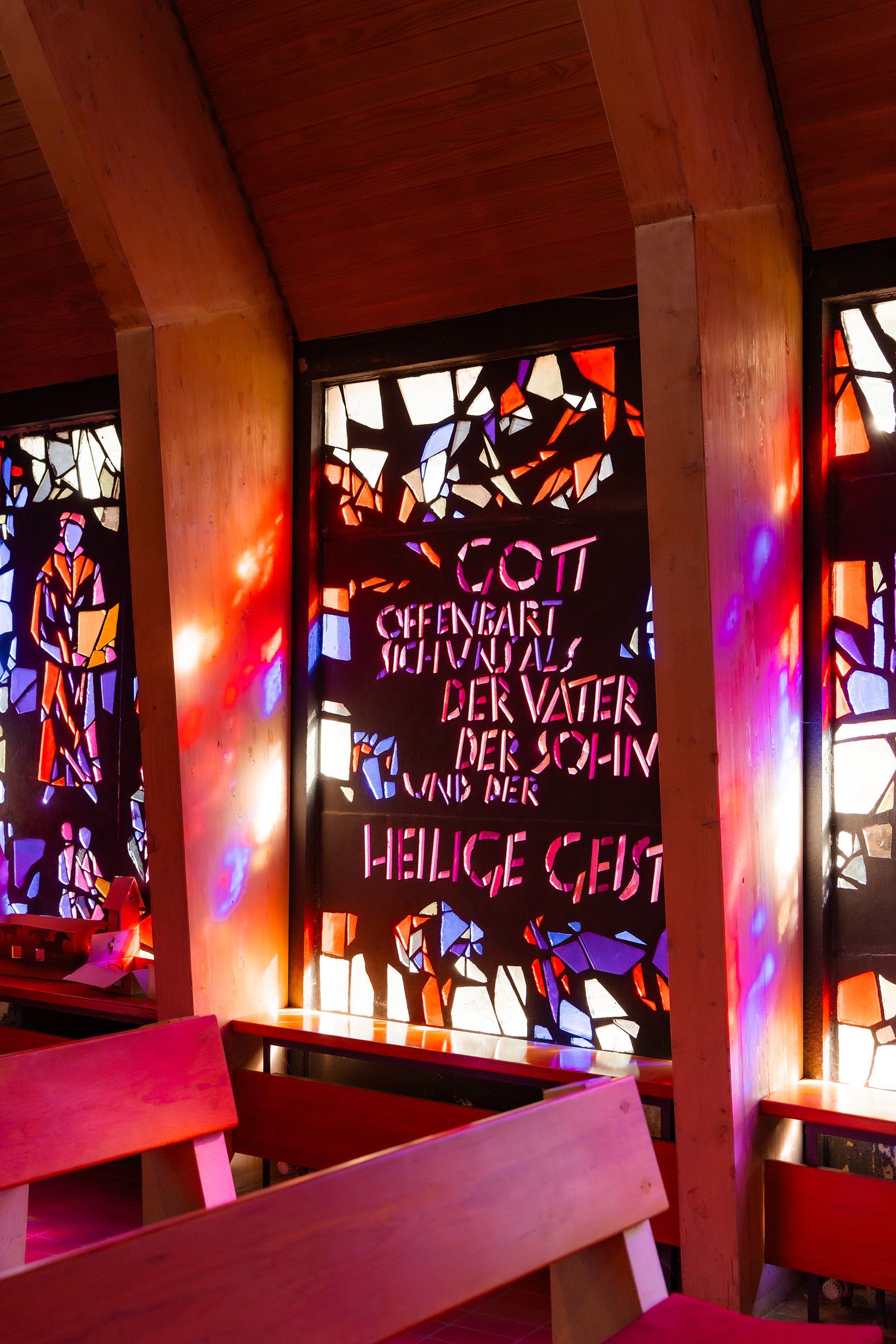 Innenaufnahme der Kirche in Bremen mit moderner Holzdecke und buntem Glasfenster, durch das Licht in warmen Farbtönen fällt.