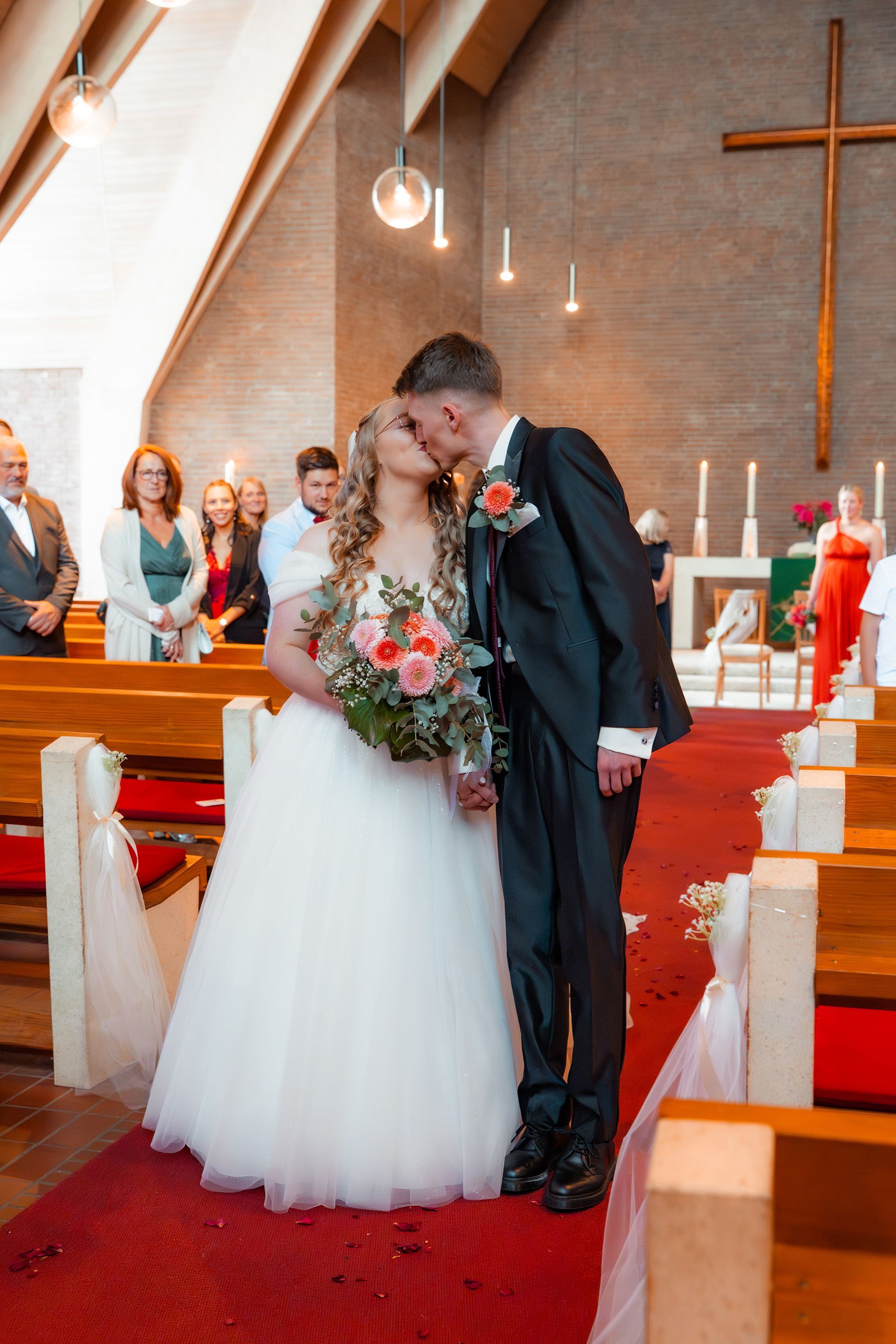 Brautpaar küsst sich beim Auszug aus der Kirche in Bremen, im Hintergrund Gäste vor dem Altar mit großem Kreuz.