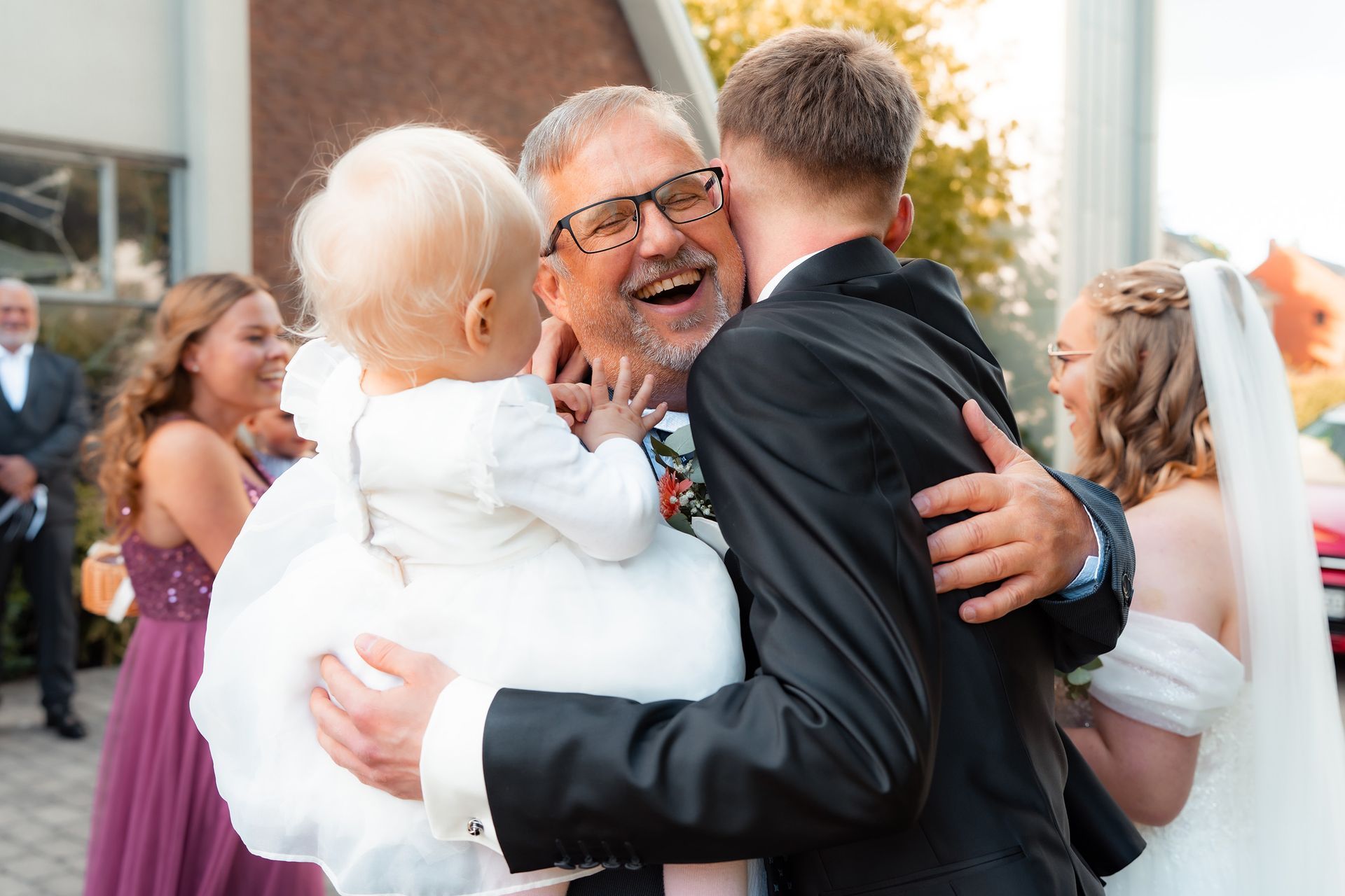 Fröhliche Umarmung zwischen Brautpaar und Familienmitglied mit Kind nach der kirchlichen Trauung in Bremen.