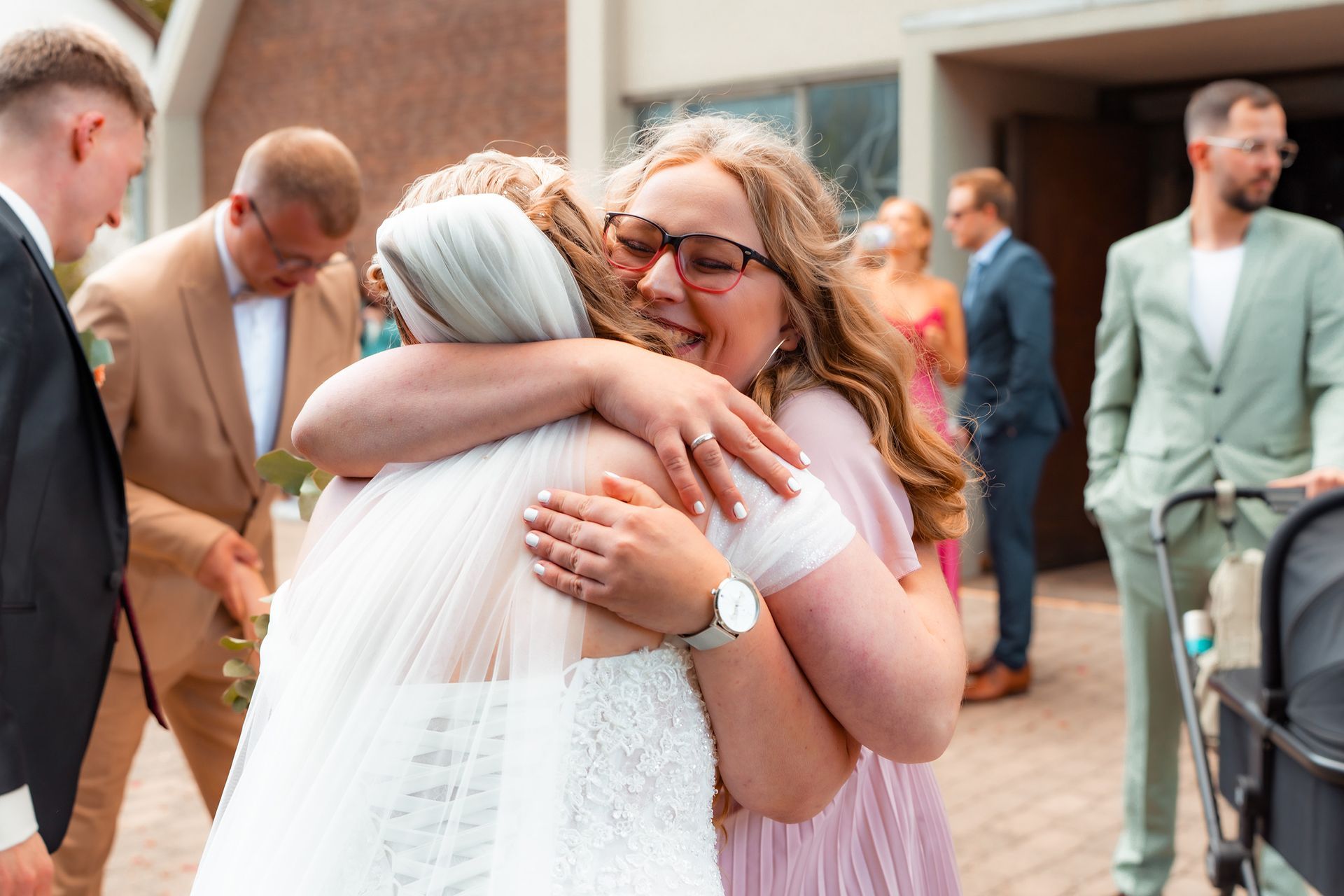 Braut wird freudig von einer Freundin nach der kirchlichen Trauung umarmt, im Hintergrund Gäste vor der Kirche in Bremen.