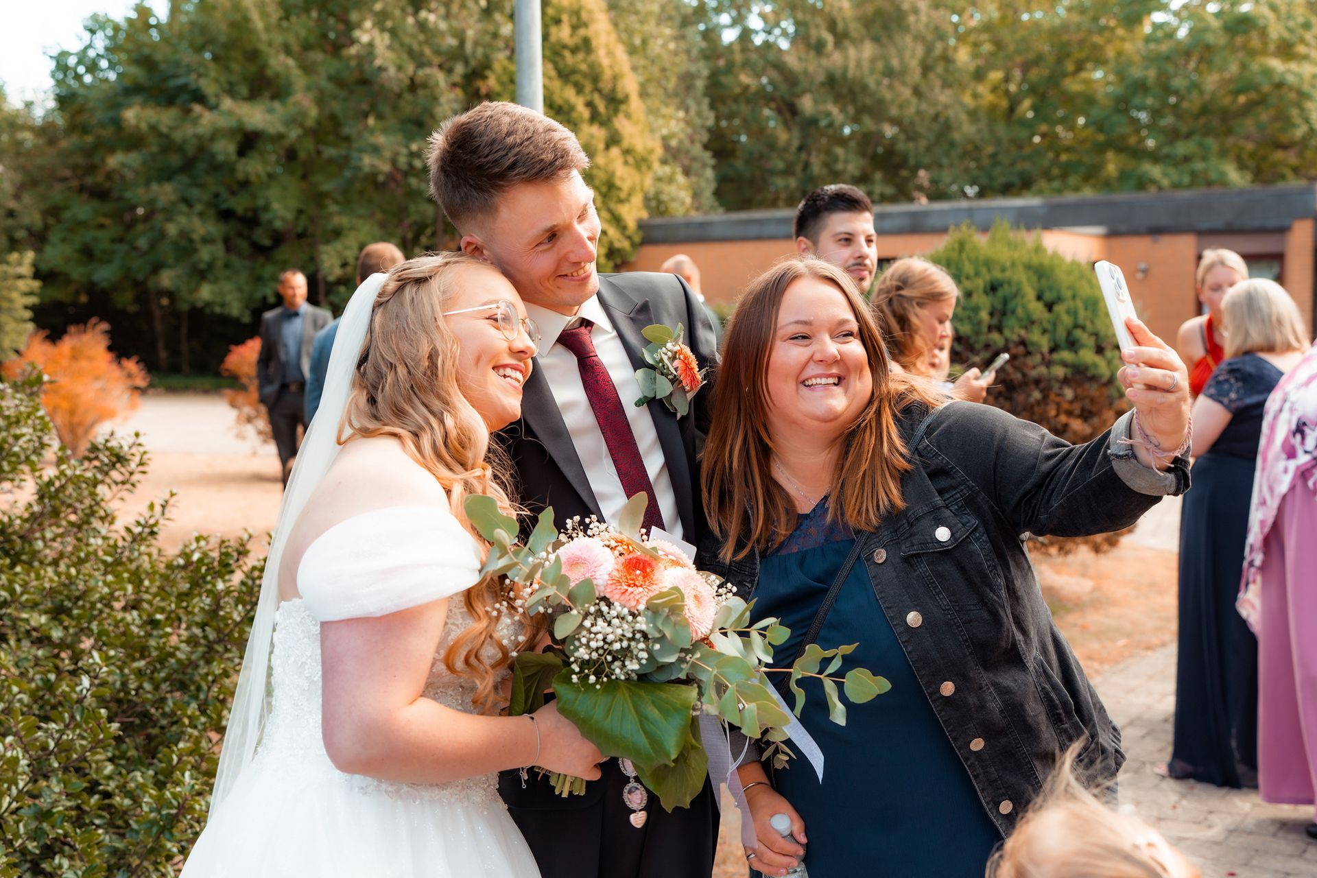 Gast macht ein fröhliches Selfie mit dem Brautpaar nach der kirchlichen Trauung in Bremen.