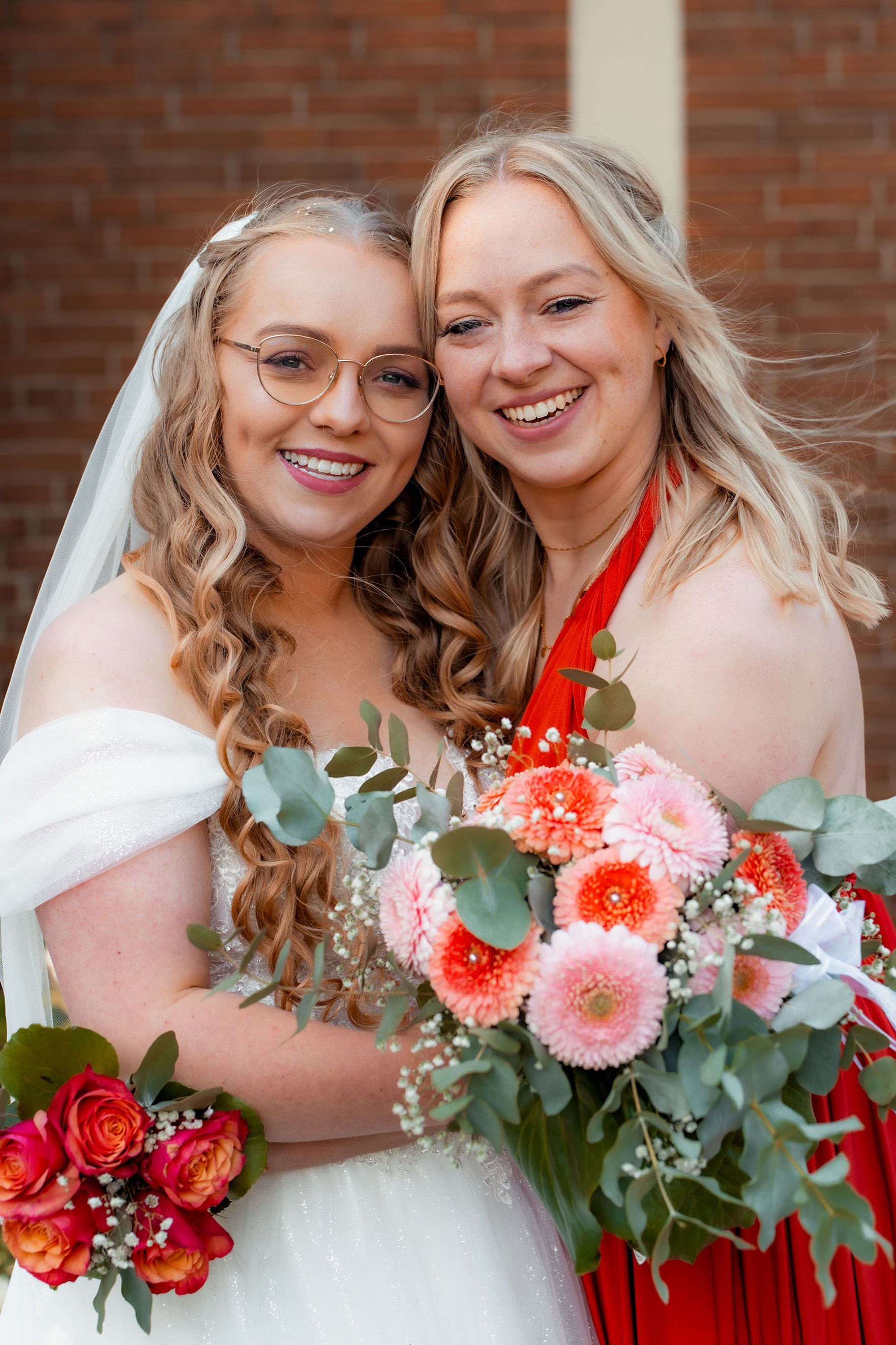 Porträt der Braut mit ihrer Schwester, beide lachend vor der Kirche nach der Trauung in Bremen.