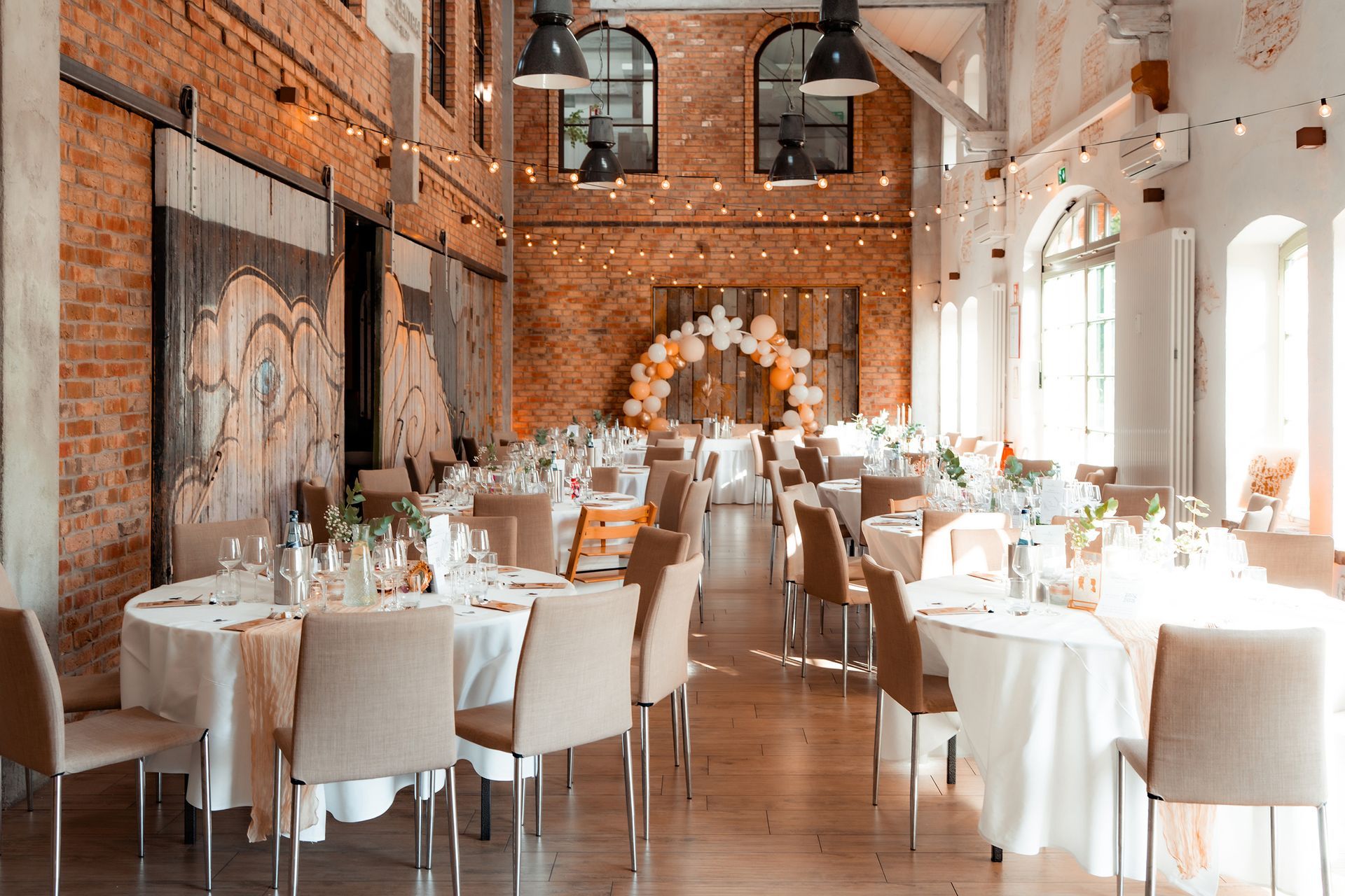 Festlich eingedeckter Hochzeitssaal im Grand Central Bremen mit rustikalem Ambiente, weißen Tischdecken und eleganten Blumen.