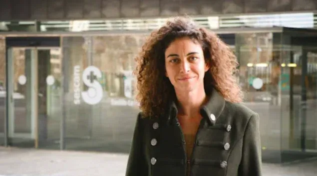 Una persona con cabello rizado y un abrigo oscuro abotonado se encuentra d