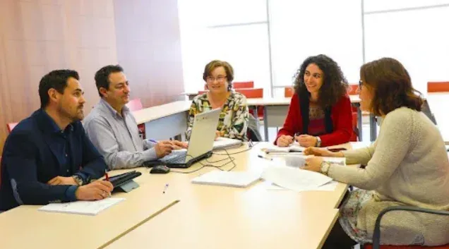 Cinco personas están sentadas alrededor de una mesa de color claro en una oficin