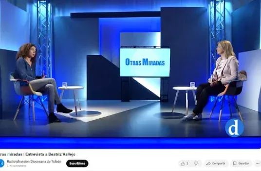 Dos mujeres están sentadas en sillas una frente a la otra en un plató de televisión