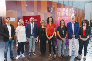 Un grupo de ocho personas posan en fila contra una pared con el logotipo de UAM, sonriendo para una foto en el interior.