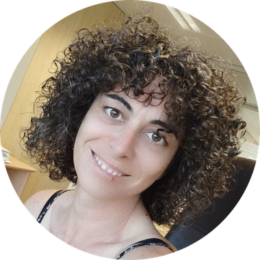 Una persona sonriente con cabello castaño rizado hasta los hombros