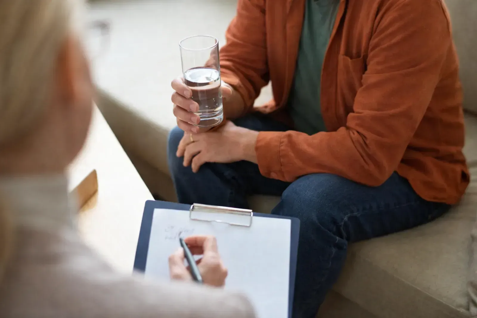 Una persona sostiene un bolígrafo sobre un portapapeles mientras mira a otra