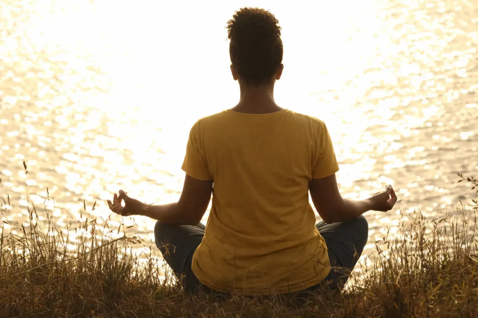 Una persona con una camisa amarilla está sentada en postura meditativa en una