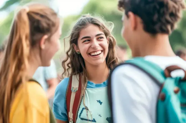 Tres estudiantes con mochilas están de pie al aire libre, riendo y charlando en un grupo amigable.