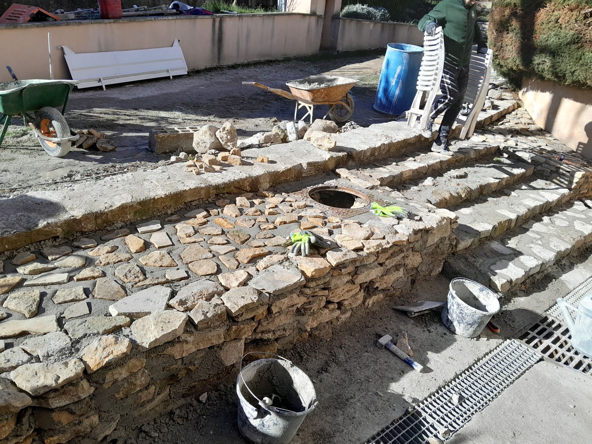 Des ouvriers construisent des murs de soutènement en pierre et des marches à l'extérieur.