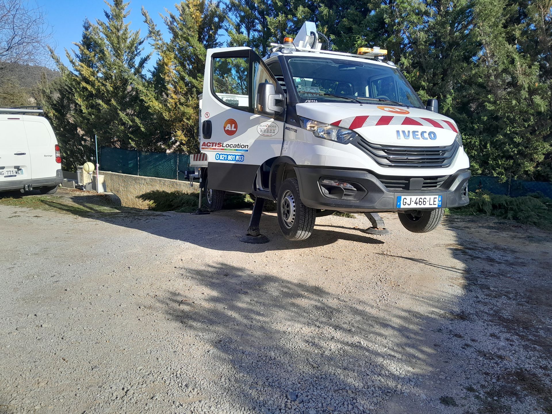 Camion de travail Iveco blanc et rouge sur du gravier ; une personne se tient à proximité avec la porte ouverte.