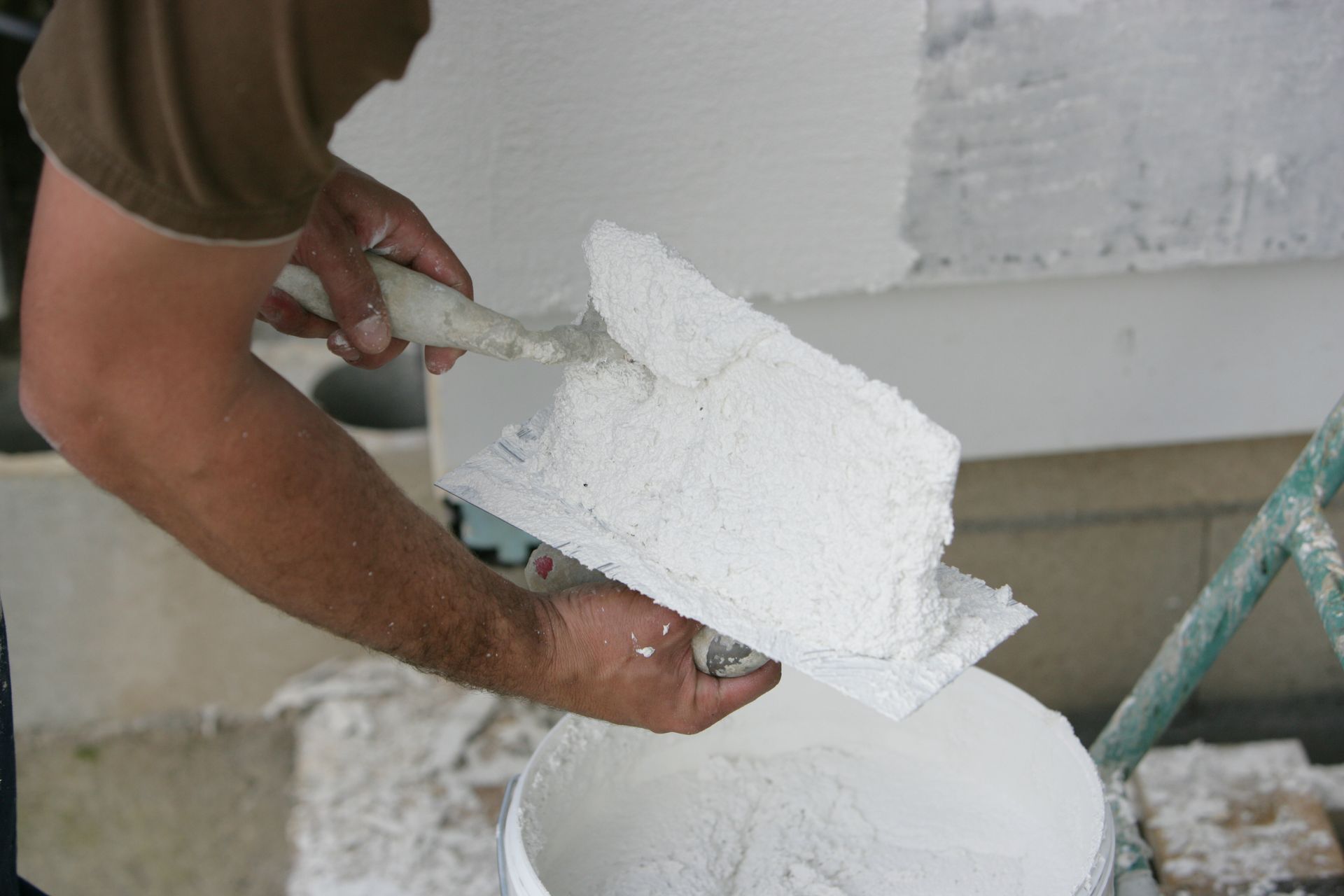 Personne appliquant du plâtre blanc avec une truelle à partir d'un seau.