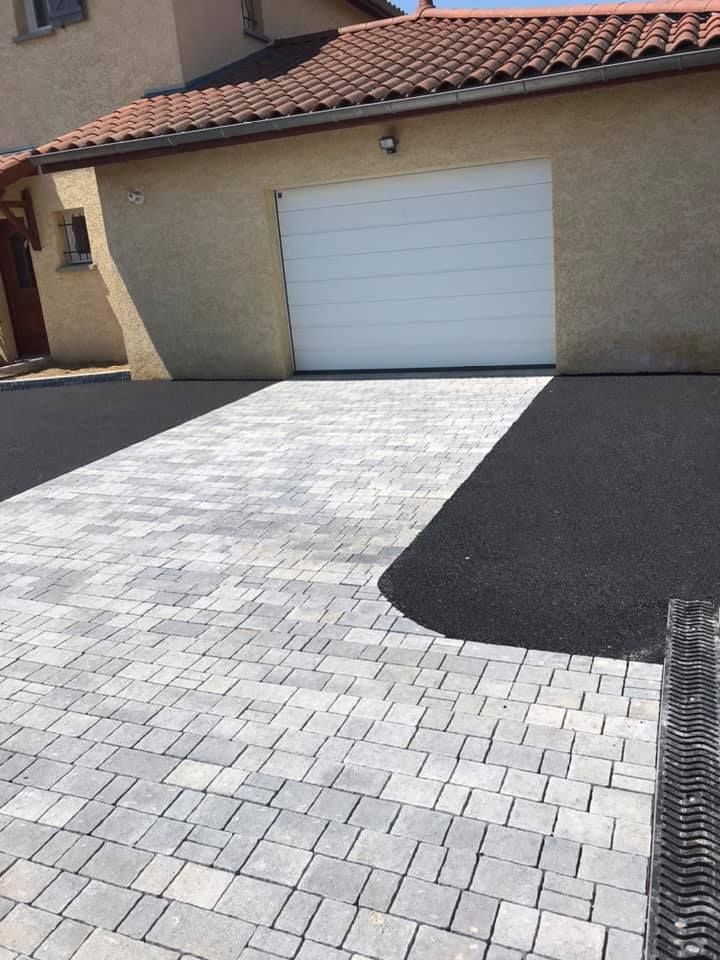 Allée pavée de dalles grises et d'asphalte noir menant à un garage avec une porte blanche.