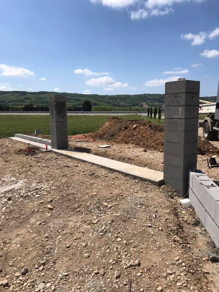 Chantier de construction avec piliers en parpaings et allée en béton, journée ensoleillée.