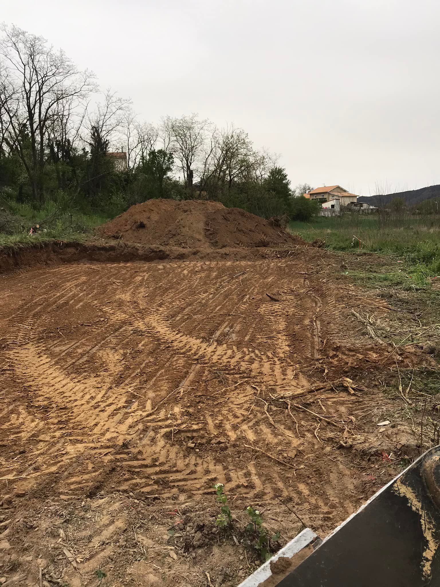 De la terre et un tas de terre sur un chantier de construction, avec des arbres et un bâtiment en arrière-plan.