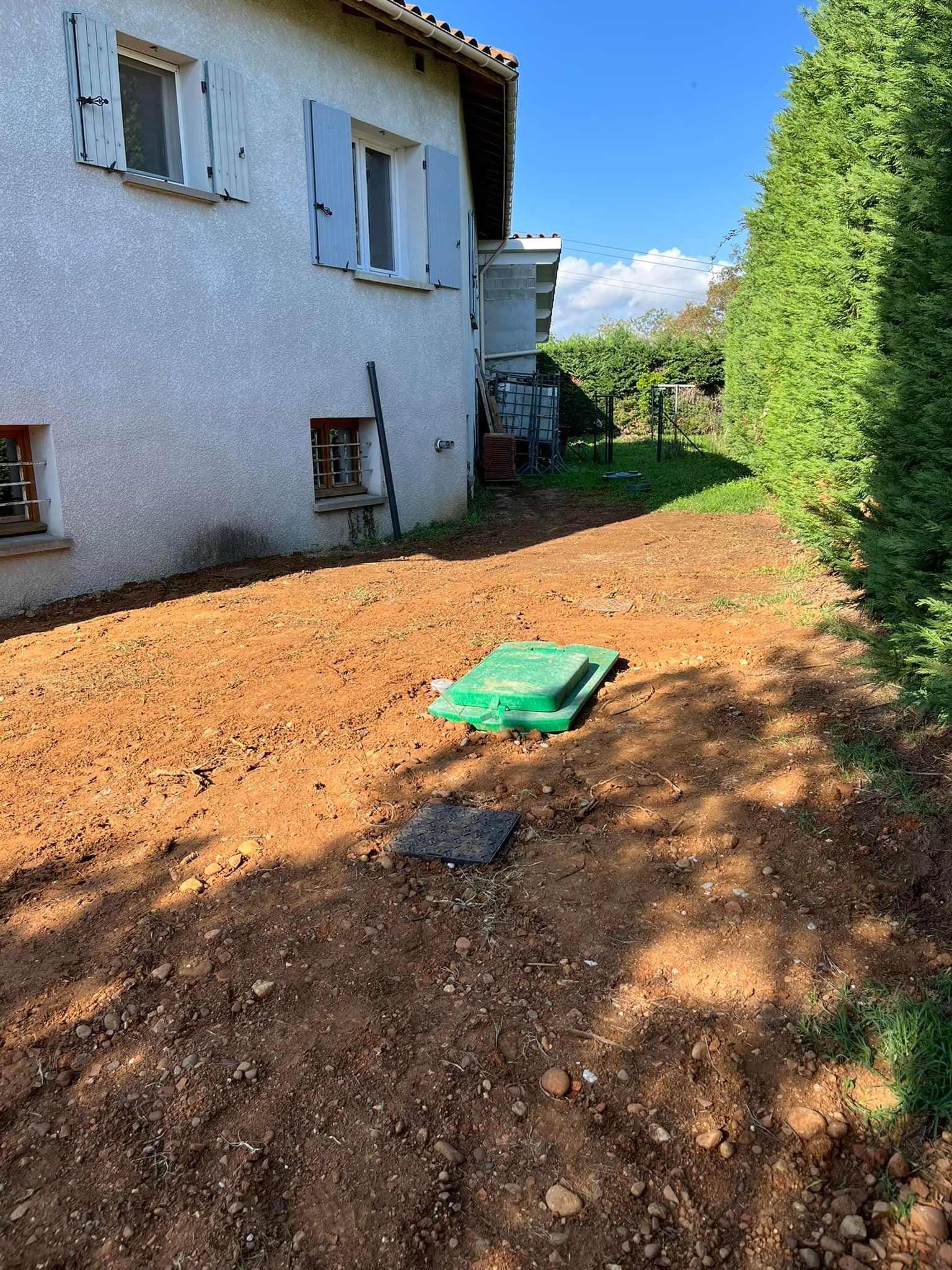 Une cour avec un sol fraîchement labouré, un abri végétalisé et une maison.