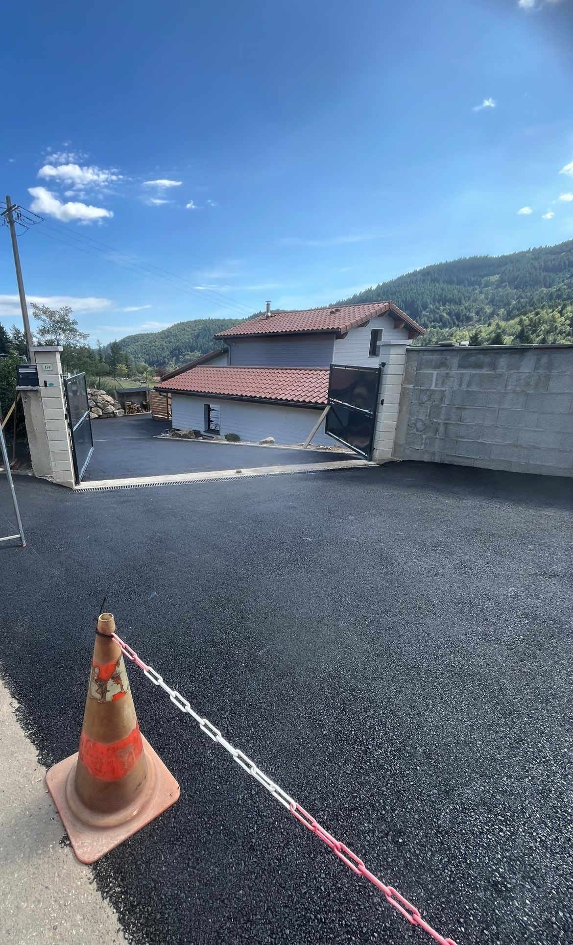 Allée nouvellement pavée menant à une maison au toit de tuiles rouges ; un cône de signalisation et une barrière de sécurité sont visibles au premier plan.