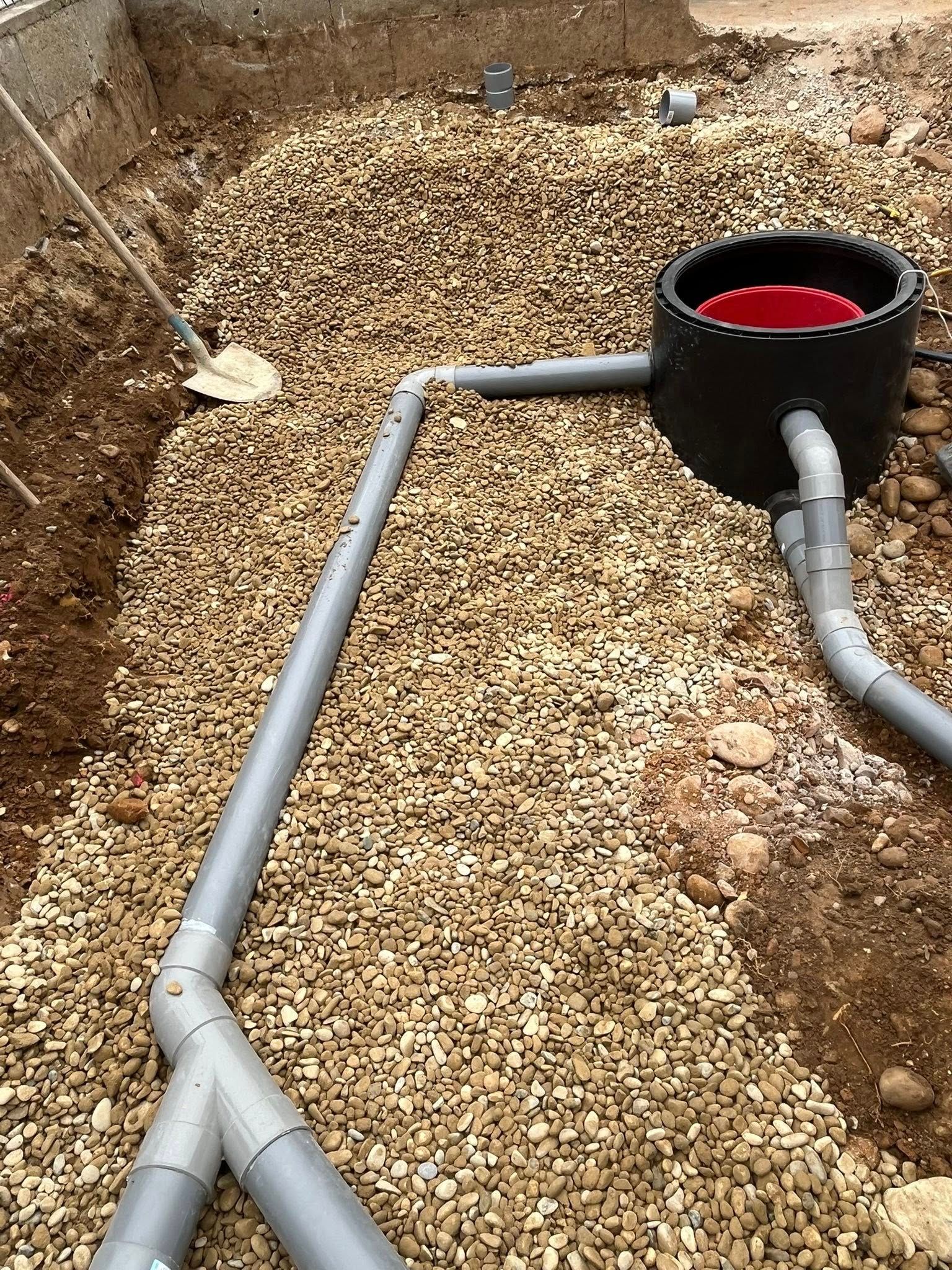 Tranchée remplie de gravier avec des tuyaux en PVC et un bassin noir pour l'installation du système de drainage.