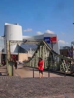 Eine Frau in einem roten Kleid geht über eine Brücke vor einem Gebäude.