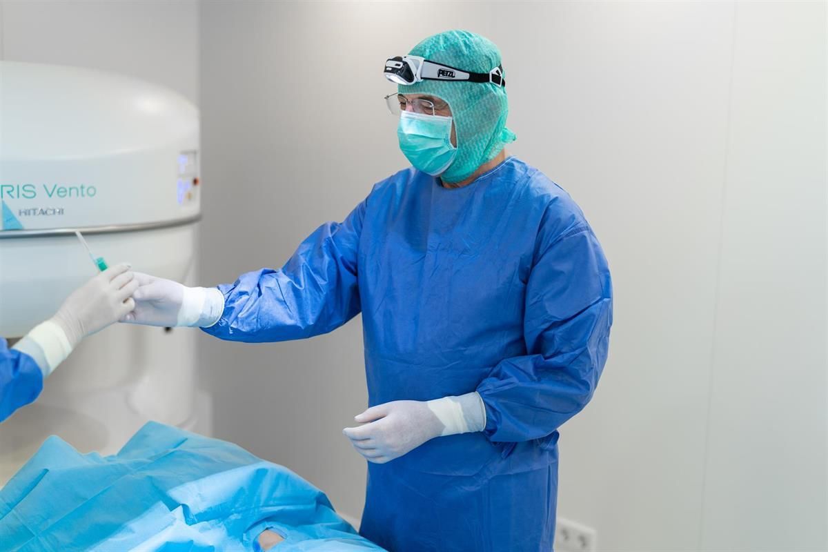 Ein Chirurg mit Maske und Kittel hält in einem Operationssaal die Hand eines Patienten.